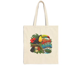 Pode incluir: Uma sacola de lona bege com um gráfico colorido de um tucano empoleirado em um galho cercado por flores e folhas tropicais. O texto "BIRDS MAKE LIFE BETTER" está impresso ao lado de uma cena de uma pequena cachoeira.
