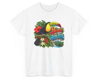 Pode incluir: Uma t-shirt branca com um gráfico colorido de um tucano pousado num ramo rodeado por flores e folhas tropicais. O texto "Birds MAKE LIFE BETTER" está impresso numa fonte estilizada sobre uma paisagem com uma cascata.
