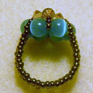 May include: A green and brown beaded ring with two large green glass beads in the centre.