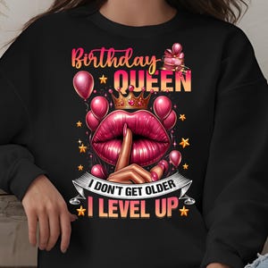 Peut inclure: Sweat-shirt noir avec un motif graphique rose et blanc qui dit "Birthday Queen I don't get older I level up".
