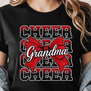 Peut inclure: Un t-shirt noir à manches courtes avec un motif graphique répétant le mot CHEER quatre fois dans une texture à paillettes rouges et noires. Un grand nœud à paillettes rouges est centré sur le texte avec le mot Grandma écrit en blanc.