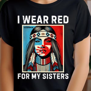 Op de afbeelding: Zwart T-shirt met witte tekst die "Ik draag rood voor mijn zussen" zegt en een hashtag die "#STOPMMIW" zegt. Het shirt heeft een afbeelding van een Native American vrouw met een rode en blauwe achtergrond.