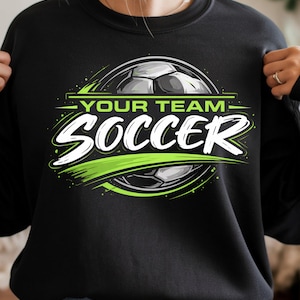 May include: Black sweatshirt with a soccer-themed graphic. The design features a soccer ball, the words "YOUR TEAM" above "SOCCER" in white, and green accents. The sweatshirt is a crew neck style.