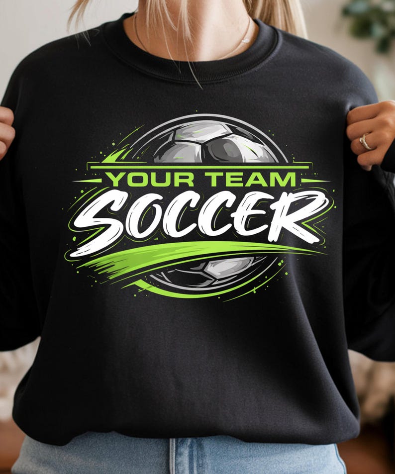 May include: Black sweatshirt with a soccer-themed graphic. The design features a soccer ball, the words "YOUR TEAM" above "SOCCER" in white, and green accents. The sweatshirt is a crew neck style.
