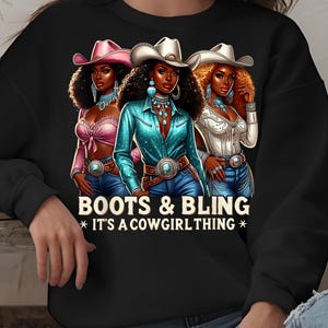 May include: Black sweatshirt with a graphic of three women wearing cowboy hats and boots. The text "Boots & Bling *It's a Cowgirl Thing*" is printed below the graphic.