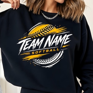 May include: Black sweatshirt with a softball design. The design features a yellow softball with white and yellow accents, and the words "TEAM NAME SOFTBALL" in white, stylized lettering.