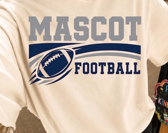 May include: A cream-colored short-sleeve t-shirt featuring the word MASCOT in large grey block letters above a graphic of a dark blue football with motion lines and the word FOOTBALL in dark blue block letters positioned below the graphic.