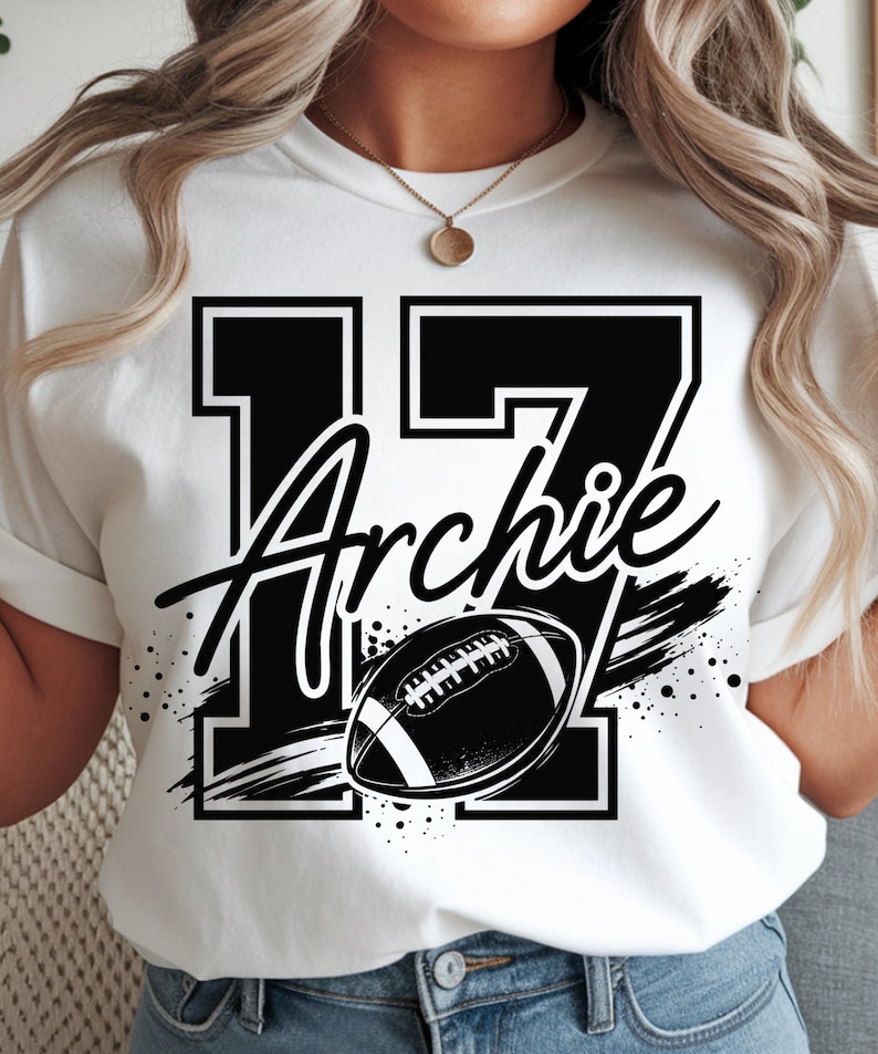 May include: A white t-shirt featuring a large black number 17 with a white outline. The name Archie is written in a black script font across the number. A black and white graphic of an American football with motion lines and paint splatters.