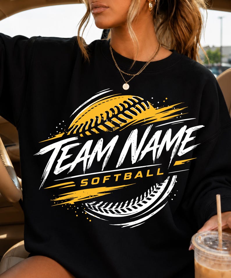 May include: A black crewneck sweatshirt featuring a graphic design with a yellow softball and white brushstroke accents. The text reads TEAM NAME in large white letters above the word SOFTBALL in smaller yellow letters, centred on the chest.