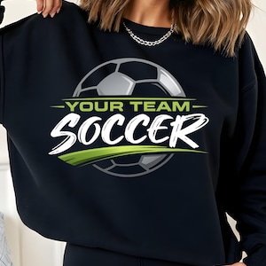 May include: Black sweatshirt with a soccer ball graphic. The design includes the words "YOUR TEAM" above "SOCCER" in white, with a green accent. The soccer ball is gray and white.