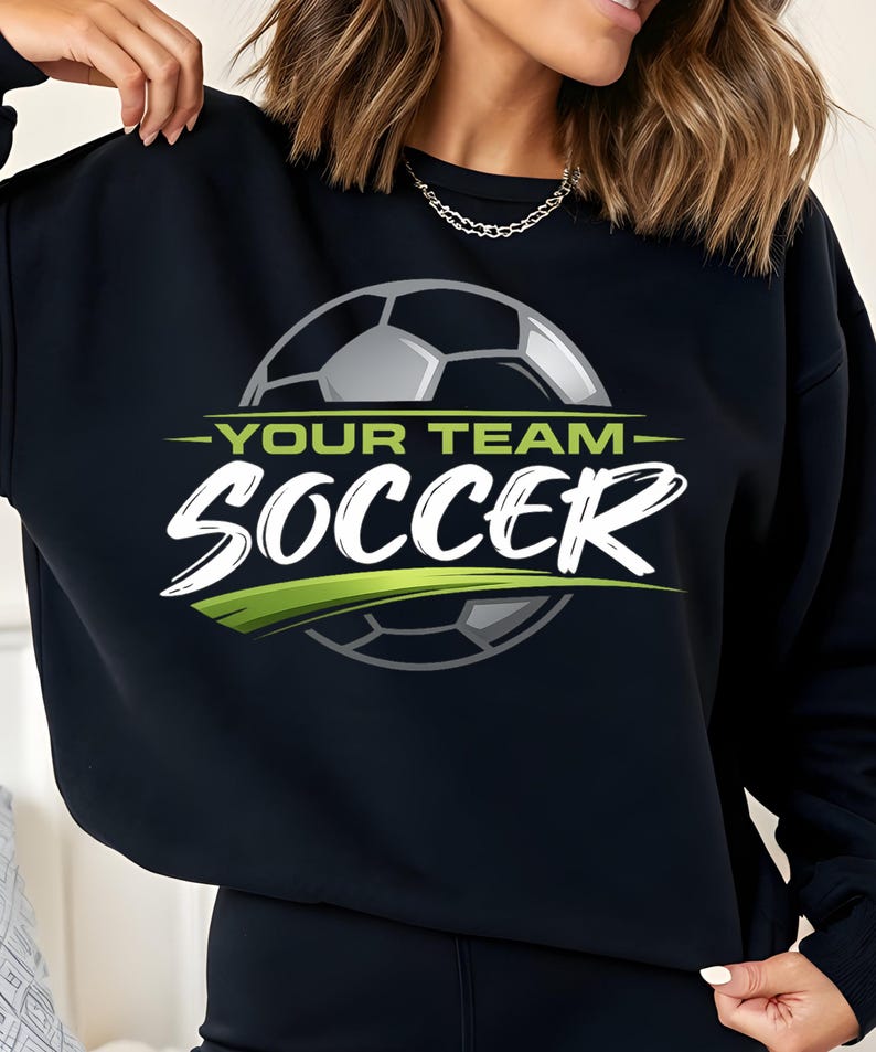 May include: Black sweatshirt with a soccer ball graphic. The design includes the words "YOUR TEAM" above "SOCCER" in white, with a green accent. The soccer ball is gray and white.