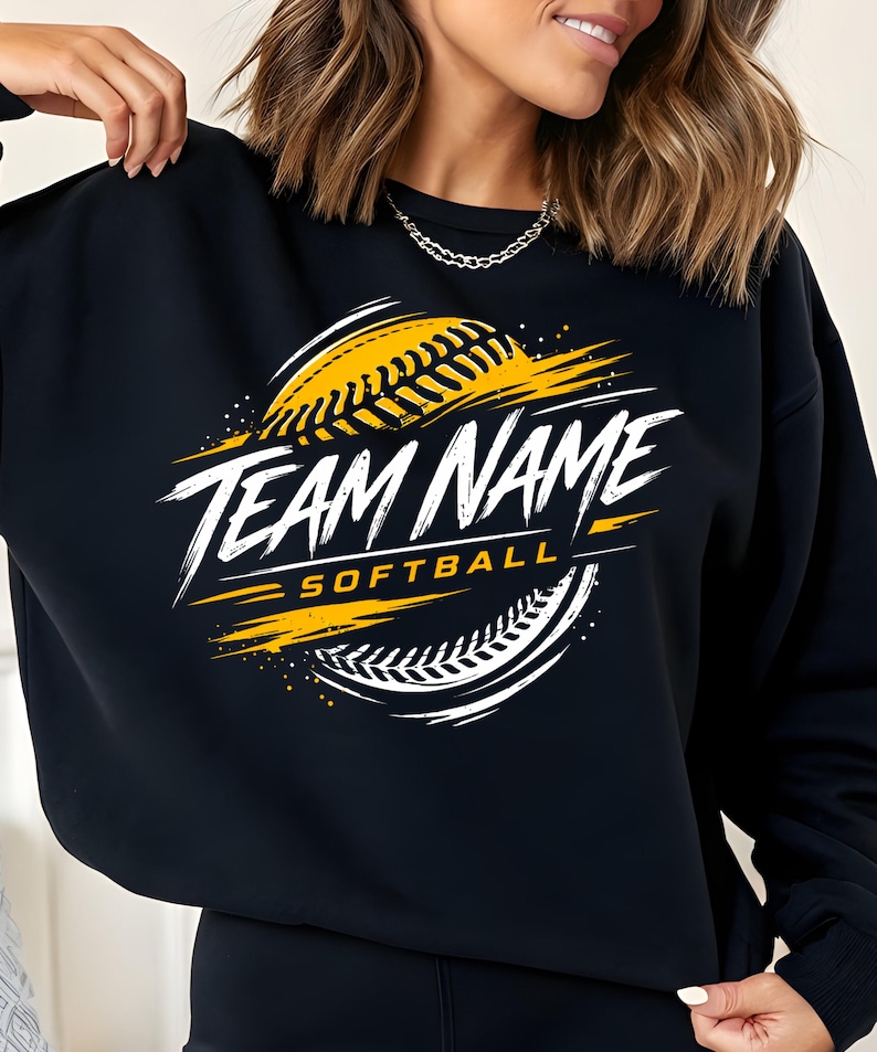May include: Black sweatshirt with a softball design. The design features a yellow softball with white and yellow accents, and the words "TEAM NAME SOFTBALL" in white, stylized lettering.
