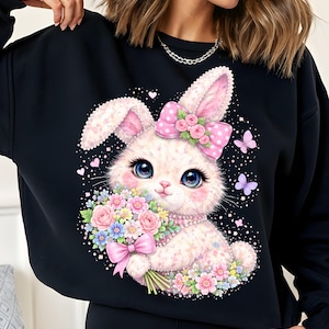 May include: Black sweatshirt with a charming bunny design. The bunny has pink ears, a polka-dot bow, and a bouquet of flowers. The design includes hearts and butterflies, creating a whimsical and festive look.