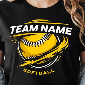 Peut inclure: T-shirt noir avec un motif de softball. Le motif comprend une balle de softball jaune avec des coutures noires, entourée de volutes jaunes et blanches. Les mots "TEAM NAME" et "SOFTBALL" sont en blanc et jaune.