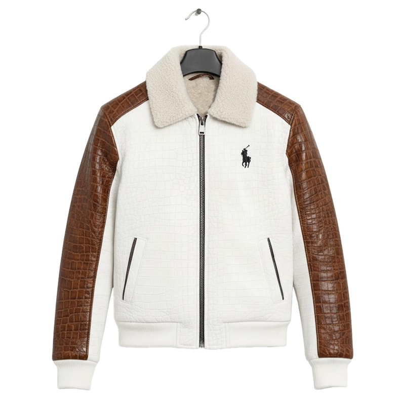 May include: White bomber jacket with brown faux-leather sleeves and a cream-colored shearling collar. Features a black zipper, two front pockets, and a black embroidered logo of a polo player. The jacket is hanging on a black hanger.