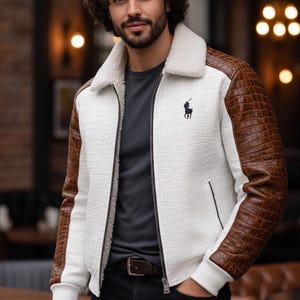 May include: White jacket with brown faux-leather sleeves and a faux-fur collar. The jacket features a black zipper, a small black logo on the chest, and a textured pattern. The jacket is paired with a dark gray shirt and black jeans.