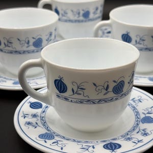 May include: Set of four white ceramic teacups with blue floral designs. The cups have a rounded shape and a small handle. Each cup is paired with a matching saucer.
