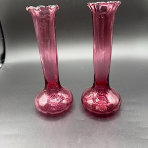 May include: A white ceramic mug with a black handle and the text "But First, Coffee" in a bold, black font. The mug is set against a blurred background, suggesting a cozy setting. The mug appears to be approximately 4 inches tall.