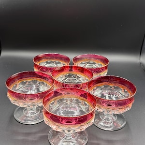 May include: Set of six clear glass dessert dishes with a red and gold rim. The dishes have a scalloped edge and a small stem.
