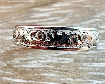 May include: A silver band ring with a decorative design of swirling leaves and stars.