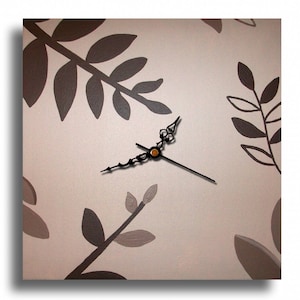 Peut inclure: Une horloge murale beige avec des aiguilles noires et un motif floral brun. L'horloge a un design simple et minimaliste.