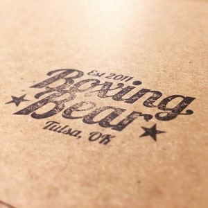 May include: A brown paper bag with a black and white logo that says "Boxing Bear" with the text "Est 2011" and "Tulsa, OK" underneath.