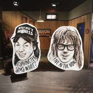 May include: Two black and white illustrations of men's faces. The first illustration features a man wearing a black baseball cap with the text "Wayne's World" on it. The text "Asphincter Says What?" is below the illustration. The second illustration features a man with long hair and glasses. The text "Live in the Now" is below the illustration.