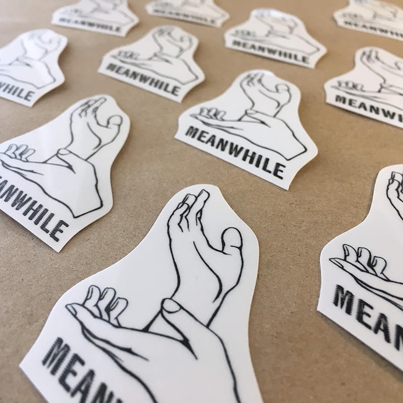 May include: A set of white stickers with a black line drawing of hands in a gesture of holding something. The stickers have the word "MEANWHILE" printed on them.