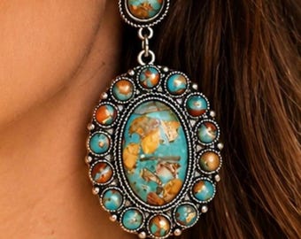 May include: A drop earring featuring a large oval centerpiece and a smaller circular top piece, both set with multicolored turquoise and copper-toned stones. The stones are surrounded by a silver-toned metal frame with a twisted rope texture.