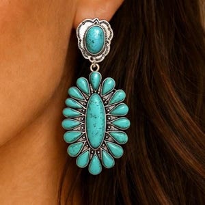Peut inclure: Gros plan sur des boucles d'oreilles turquoise et argentées. Les boucles d'oreilles ont un motif floral avec une grosse pierre turquoise au centre et de petites pierres turquoises autour. Les boucles d'oreilles pendent.