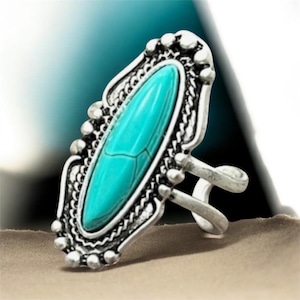 May include: Silver-toned ring featuring an oval, turquoise-colored stone. The ring has an ornate, filigree-style setting with beaded and textured details. The band splits into two parts before joining the setting.
