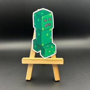 May include: A green Minecraft Creeper sticker on a small wooden easel.