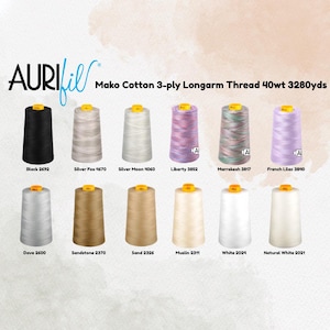 May include: A selection of Aurifil Mako Cotton 3-ply Longarm Thread spools in various colors. The image displays spools in shades of black, gray, white, pink, green, purple, and beige. Each spool is labeled with a color name and number. The text "Mako Cotton 3-ply Longarm Thread 40wt 3280yds" is at the top.