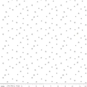 Pode incluir: Tecido branco com um padrão disperso de pequenas estrelas cinzentas. As estrelas são uniformemente espaçadas na superfície. O tecido tem uma régua ao longo da borda inferior, medida em polegadas.