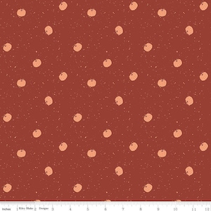 May include: A dark red fabric featuring a repeating pattern of small, light orange pumpkins and tiny white speckles. A white ruler at the bottom edge shows a scale of 12 inches, with the text Riley Blake Designs printed near the left side.