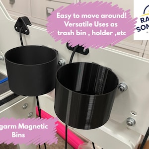 May include: Two black plastic bins with long arms and magnetic bases. The bins are attached to a white surface and are labeled "Longarm Magnetic Bins". The text "Easy to move around! Versatile Uses as trash bin, holder, etc" is written in pink on a white background. The text "RAY OF SONSHINE DESIGN" is written in white on a yellow circle with a sun graphic.