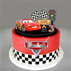 May include: A red birthday cake decorated with a Lightning McQueen car, checkered flags, and a traffic light. The cake has a red base with a black and white checkered border and the name "Isaiah" on the front.