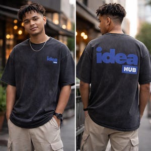 A young man wearing a black t-shirt with the word "IDEA" printed on it, standing in front of a building.