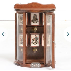 May include: A wooden curio cabinet with glass doors and shelves. The cabinet is filled with small, framed clocks with different designs. The cabinet has a curved front and a dark wood finish.