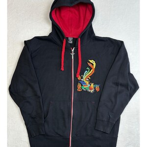 Op de afbeelding: Zwarte hoodie met ritssluiting en een rood gevoerde capuchon. De hoodie heeft een kleurrijk geborduurd feniksontwerp op de voorkant. De rits is zilverkleurig en de trekkoorden zijn rood.