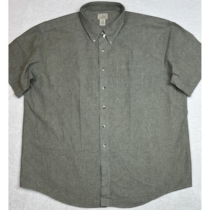 Könnte beinhalten: Graues kurzärmeliges Hemd mit Button-Down-Kragen und Brusttasche. Das Hemd hat eine Knopfleiste und ein kleines Logo in der Nähe des Kragens. Der Stoff scheint ein gewebtes Material zu sein.