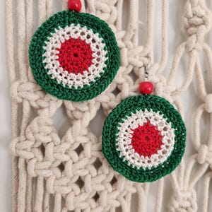 Peut inclure: Une paire de boucles d'oreilles en crochet avec un motif rouge, blanc et vert. Les boucles d'oreilles sont rondes et ont un design en cercles concentriques.