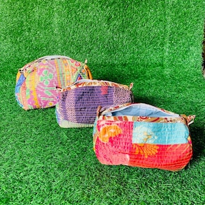 Op de afbeelding: Drie kleurrijke, patroonrijke make-up tassen met ritssluitingen. De tassen zijn gemaakt van patchwork stof in tinten roze, paars, blauw en oranje. Ze zijn gerangschikt op een groen oppervlak.