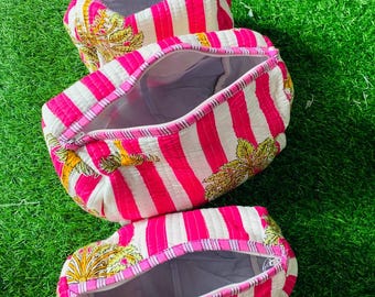 Pode incluir: Três bolsas de cosméticos abertas, com padrão de listras rosa e branco. As bolsas têm fecho de zíper e um desenho floral nas extremidades. As bolsas estão em uma superfície verde.
