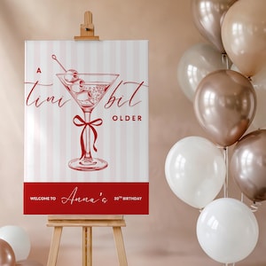 May include: A red and white striped sign with the text "A tiny bit older" and a martini glass illustration. The sign also says "Welcome to Anna's 30th Birthday".