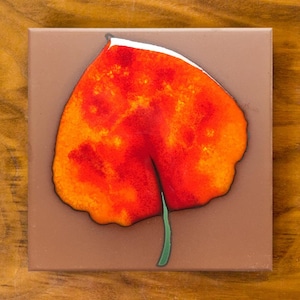 May include: Square ceramic tile featuring a vibrant, stylized leaf design. The leaf is primarily red and orange with white accents, set against a brown background. A green stem completes the botanical image, suitable for home decor.