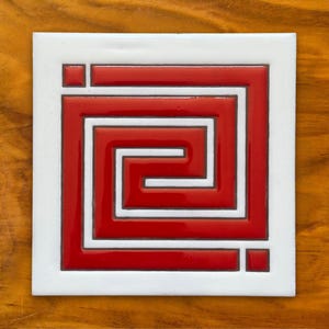 May include: A white ceramic tile with a red Greek key design. The design is raised and has a glossy finish.
