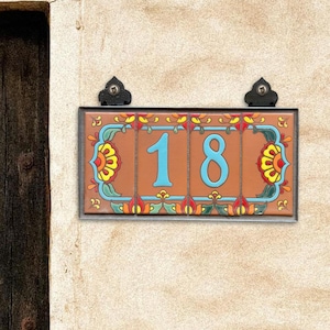 May include: A terracotta tile house number sign with a colorful floral design. The number 18 is displayed in blue on a terracotta background.