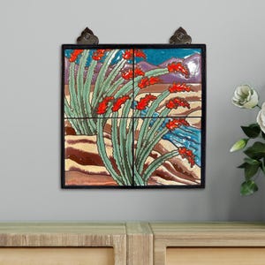 May include: A framed tile art piece featuring a desert landscape with red flowering plants, green cacti, and a blue river. The artwork is composed of four tiles and is mounted on a wooden surface.
