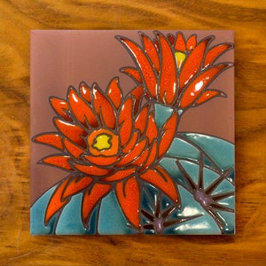 May include: A ceramic tile with a hand-painted design of two red and orange cactus flowers with green and purple accents.